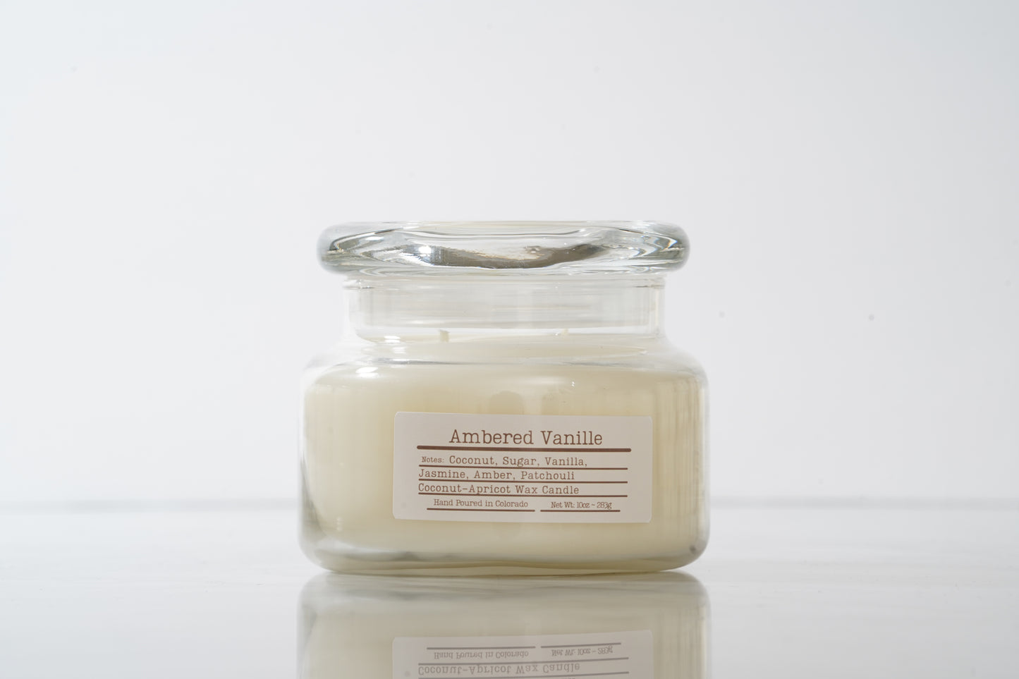 Glass candle jar labeled 'Ambered Vanilla' on a white background