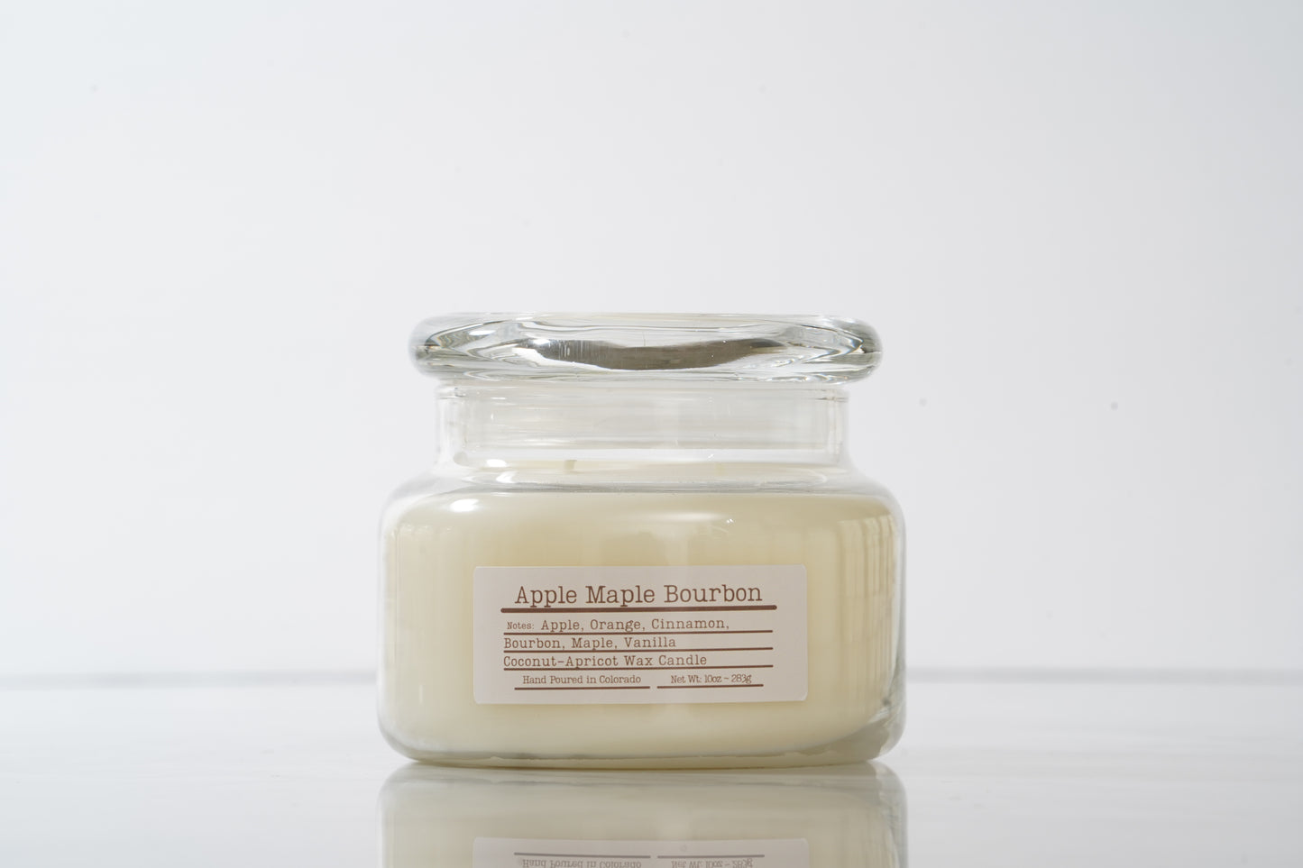 Glass candle with 'Apple Maple Bourbon' label on a white background
