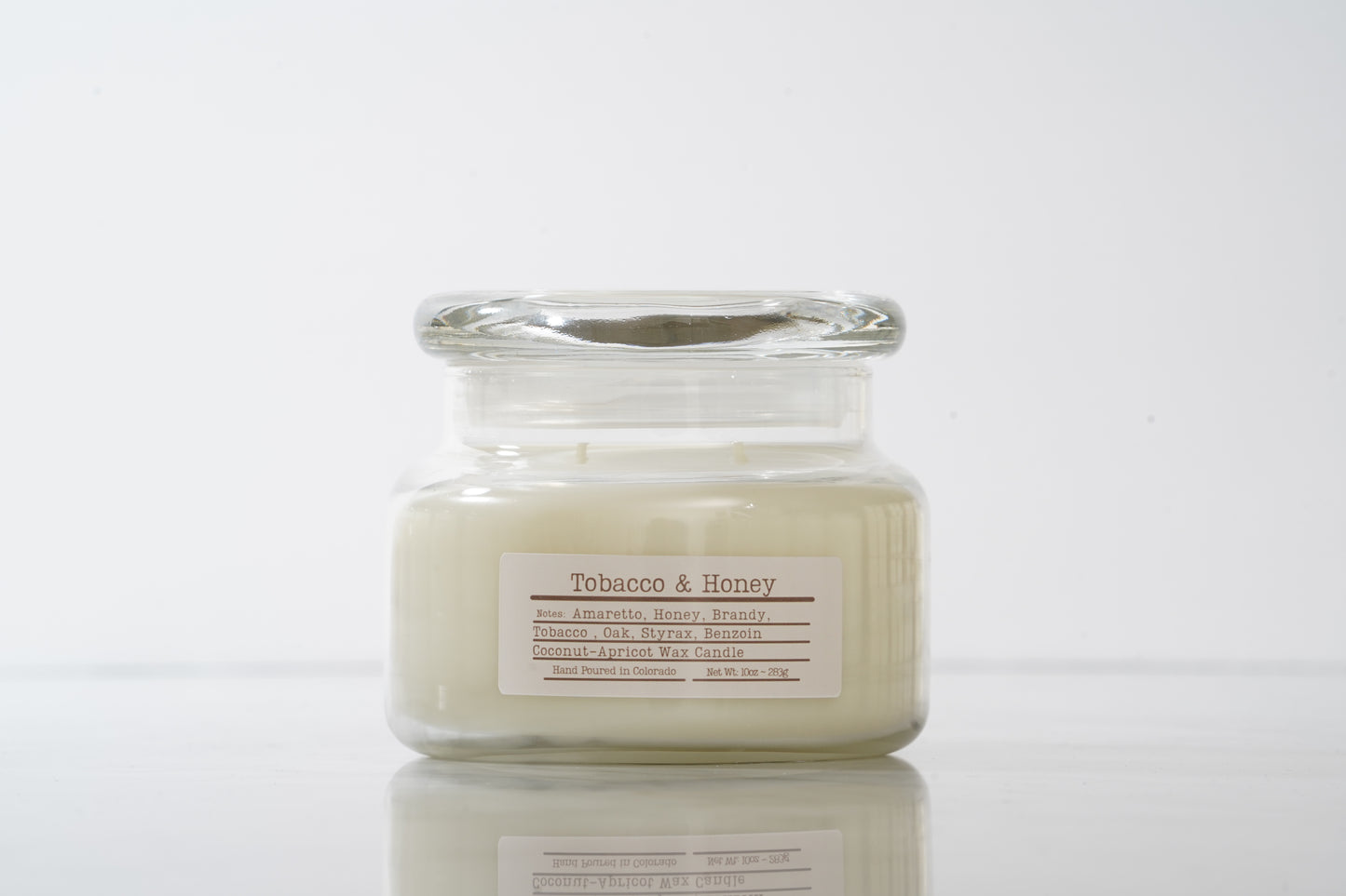 Candle in a glass jar labeled 'Tobacco & Honey' on a white background