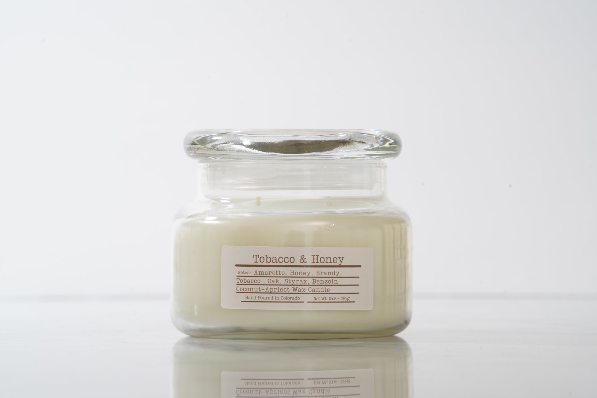 Candle in a glass jar labeled 'Tobacco & Honey' on a white background