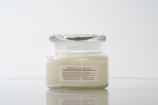 Candle in a glass jar labeled 'Tobacco & Honey' on a white background